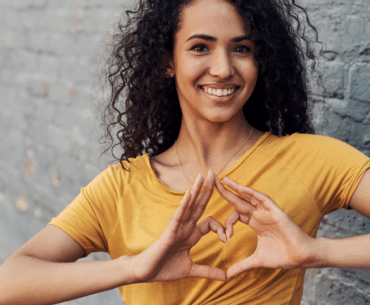 Woman in gold shirt making heart with hands