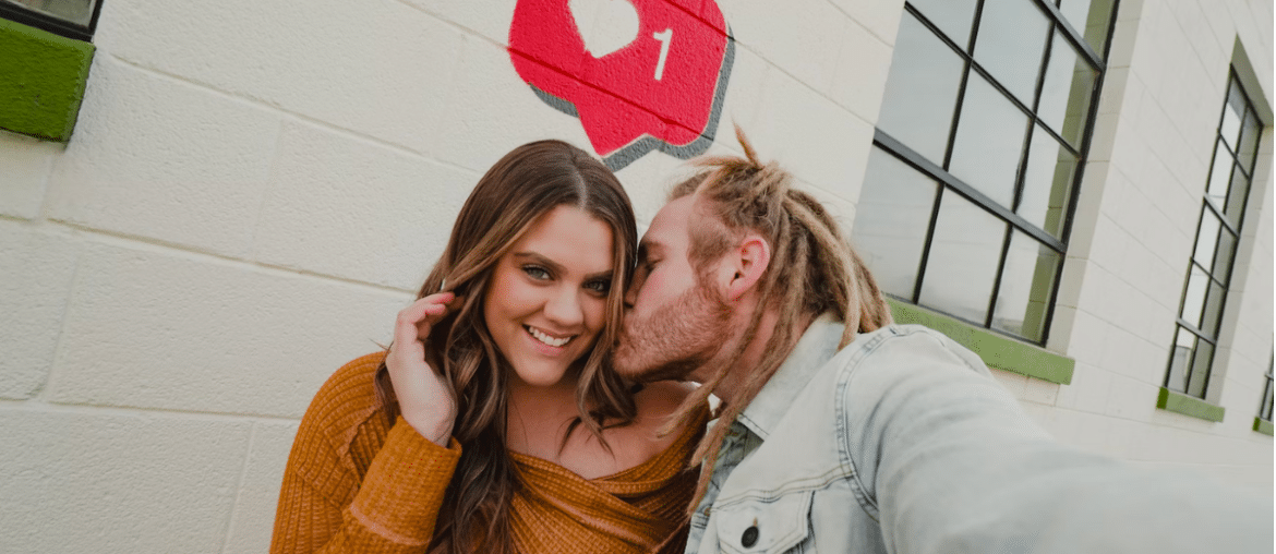 A man kissing a woman on the cheek with a like symbol behind them