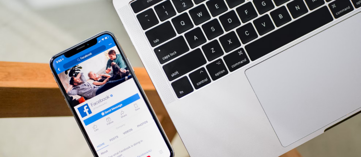 A phone with Facebook. on the screen next to a laptop